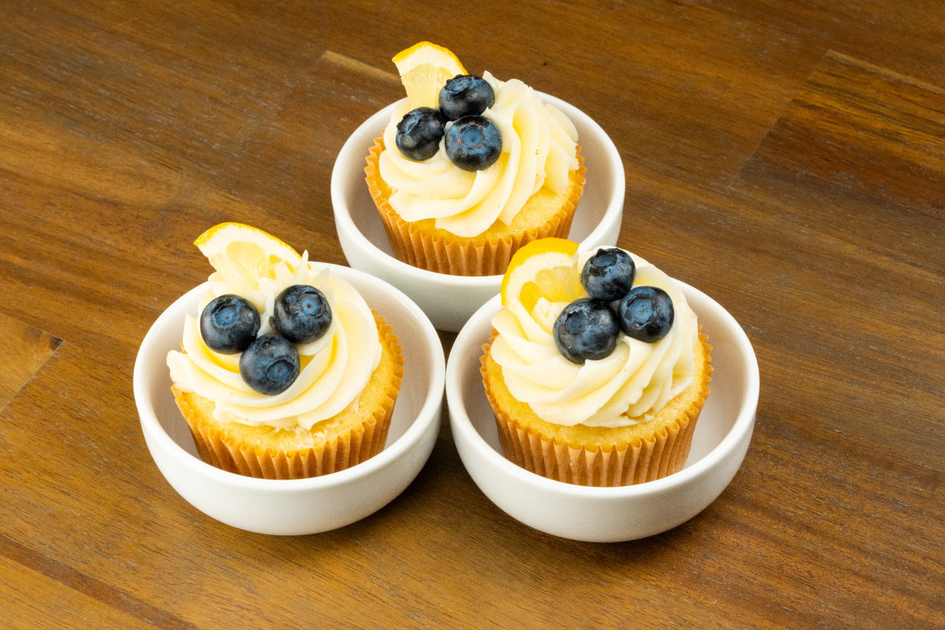 Three lemon blueberry cupcakes served in small white bowls on a walnut table