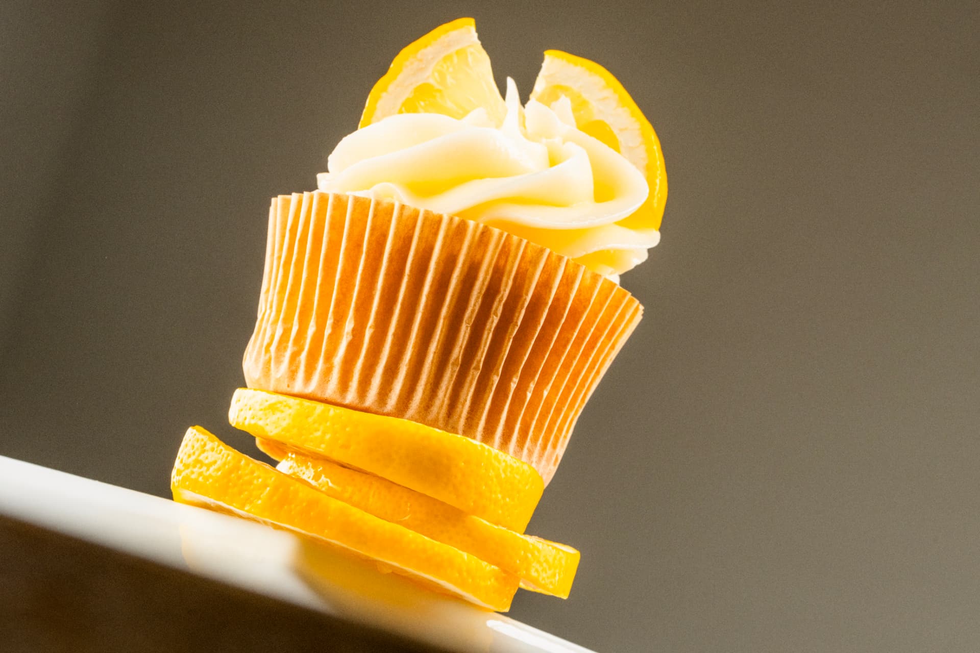 Lemon cupcake tilted on a white plate with curled lemon peel beneath it