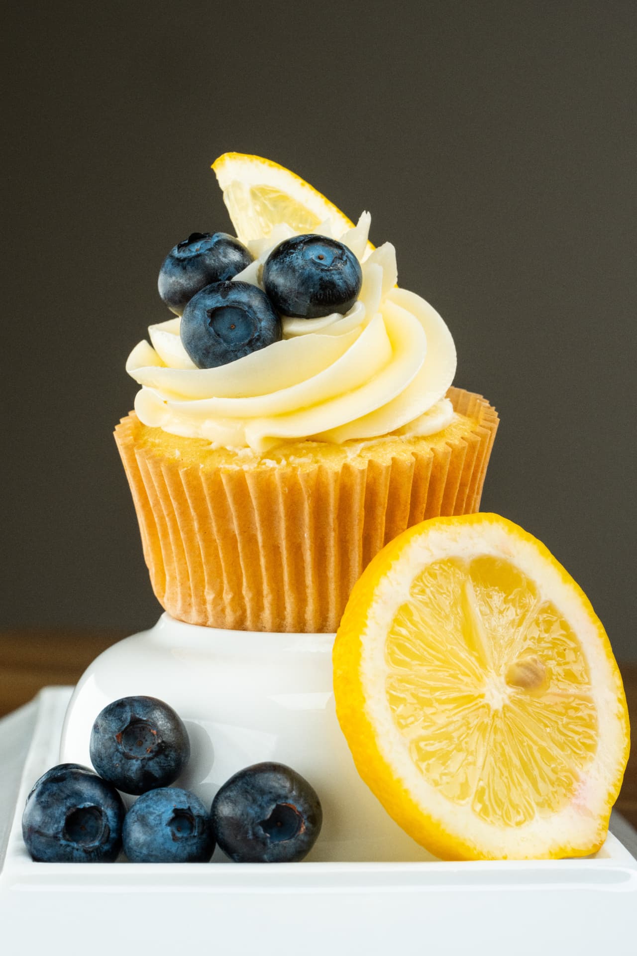 Lemon cupcake topped with cream cheese frosting, fresh blueberries, and a lemon wedge