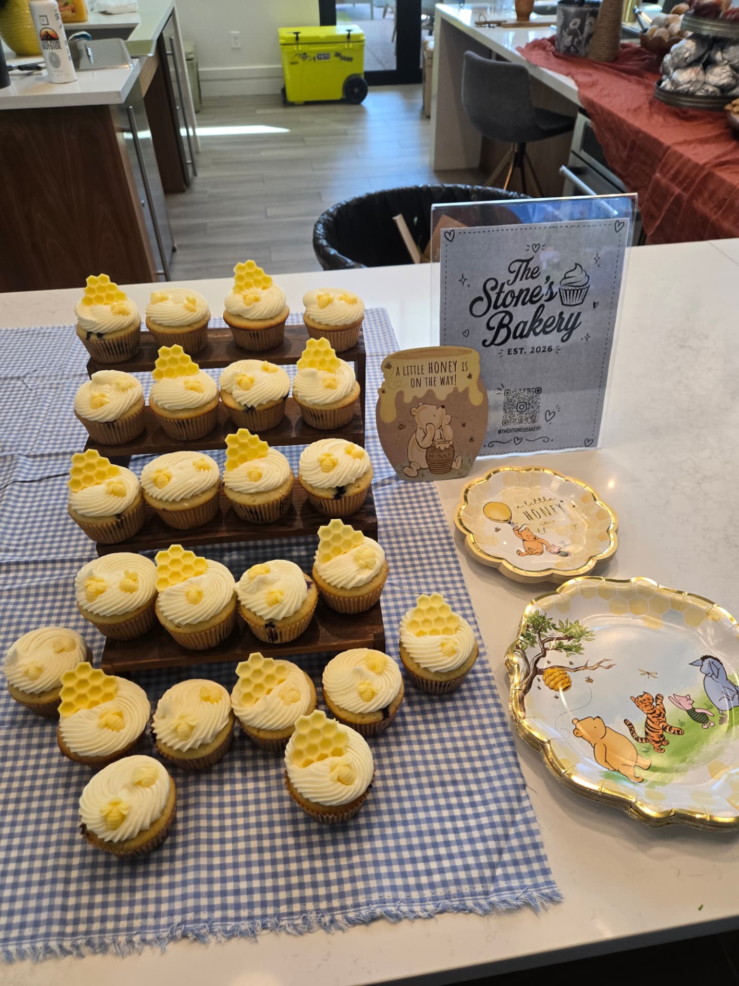 Honey-themed cupcake display with honeycomb toppers beside bakery signage and party plates