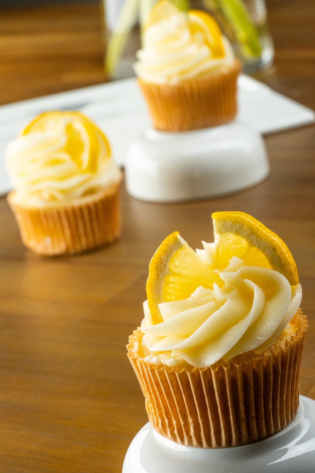 Three lemon cupcakes with buttercream swirls and lemon wedges arranged on a dark wood table
