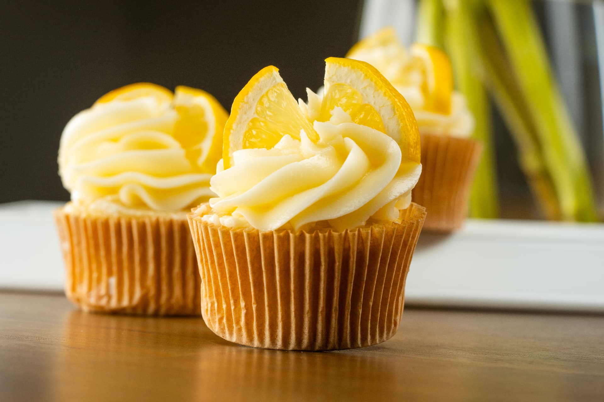 A row of lemon cupcakes topped with buttercream swirls and fresh lemon wedges